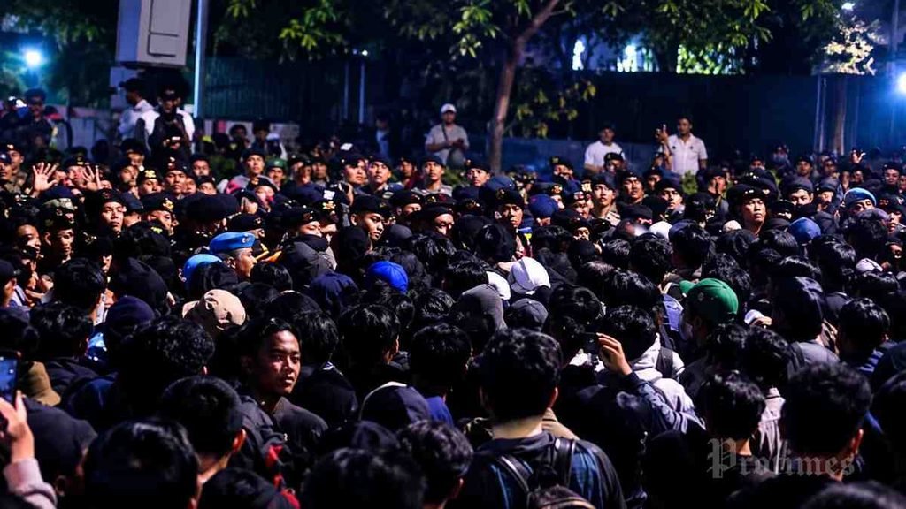 Massa aksi mahasiswa berkumpul pada malam hari dalam demonstrasi di Indonesia, dengan aparat keamanan berjaga di hadapan kerumunan.